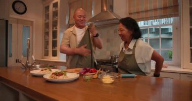 Üst düzey Asyalı çift mutfakta birlikte yemek yapmayı, evde kahkaha ve şarap paylaşmayı seviyor. Yaşlılar, birliktelik, ev hayatı, boş zaman, mutluluk, kaynaşma