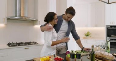 Çiftler kucaklaşırken erkekler şarapla yürür, biber doğrar ve evde salata karıştırır. Romantik, çift, yemek pişirme, modern, mutfak, sebze, hazırlık