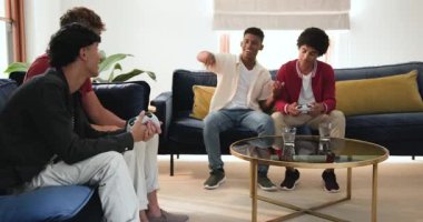 Deniz mavisi koltuklarda oturan çeşitli erkek arkadaşlar maç kazanmak için hızla oyun kontrolörlerine vurmaya başlıyorlar. Gündelik, eğlence, etkileşim, yoldaşlık, modern, enerjik, eğlence