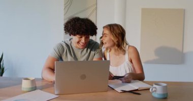 Evde sevinçle kucaklaşan genç bir çift, dizüstü bilgisayar ve defterler masanın üzerinde. ilişki, aşk, mutluluk, birliktelik, evcil, memnuniyet