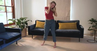 Oturma odasında kulaklıkla dans eden, müzikten hoşlanan ve evde neşe saçan genç bir kız. Rahatlama, teknoloji, ifade