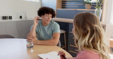 Genç çift mutfak masasında planlarını tartışıyor ellerinde defter ve bir bardak su tutuyorlar. planlama, tartışma, takım çalışması, yaşam tarzı, ilişkiler, iletişim