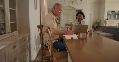 Üst düzey Asyalı çift evde dizüstü bilgisayar ve not defteri kullanarak finansman tartışıyor, kahvenin tadını çıkarıyor. Emeklilik, bütçe, planlama, yaşlılık, iletişim, yaşam tarzı