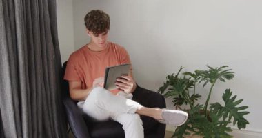 Meraklı sürücü evdeki koltukta tıkırdayıp tableti kaydırıyor, skor güncellemesini kutluyor. Modern, yaşam tarzı, minimalizm, teknoloji, rahatlama, başarı, gelişigüzel