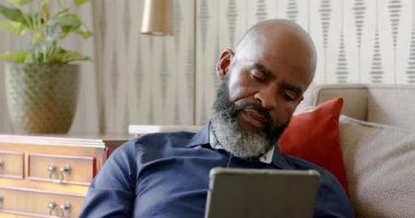 Olgun Afro-Amerikalı adam, tablet metni tarıyor, yer değiştiriyor, oturma odasındaki kanepede sızıyor. Rahatlama, teknoloji, konfor, uyku zamanı, boş zaman, yerli, modern
