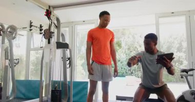 Modern spor salonunda eğitmeniyle çömelme hareketleri yapan Afrikalı Amerikalı bir adam. Spor, spor, spor, egzersiz, çömelme, motivasyon.