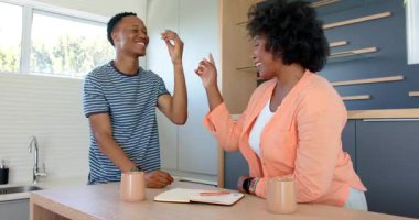 Genç Afro-Amerikan çift, evde mutfak masasında kupayla gülüp sarılıyorlar. Romantizm, yaşam tarzı, sevgi, bağlılık, aşk, sabah