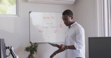 Ofiste, beyaz tahtada iş planını tartışırken tablet kullanan bir adam. toplantı, işbirliği, beyin fırtınası, teknoloji, planlama, takım çalışması