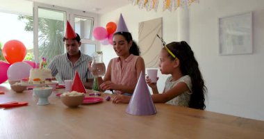 Çeşitli aileler evde, dekore edilmiş odada doğum günü partisini kutluyor, pasta ve parti şapkalarının keyfini çıkarıyorlar. Kutlama, şenlik, toplanma, atıştırmalıklar, canlı, neşeli, süslemeler, birliktelik