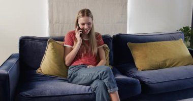 Telefon eden bir kadın, elinde akıllı bir telefonla kanepede gülüyor sonra kutlama için tablet kaydırıyor. Yaşam tarzı, rahatlama, teknoloji, konfor, mutluluk, konfor, iletişim