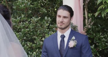 Bahçedeki pembe kemerin altında, gelin yeminlerini okuyor ve damat gülümsüyor. Romantizm, kutlama, sükunet, zarafet, mutluluk, yakınlık, şefkat