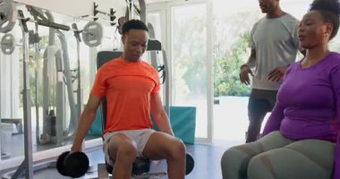 Beden eğitiminde destek veren arkadaşlarıyla ağırlık kaldıran genç bir adam. Fitness, egzersiz, güç, takım çalışması, motivasyon, eğitim