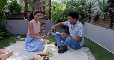 Çeşitli çiftler bahçede kadeh kaldırırken ellerinde meyve tabağıyla piknik battaniyesi tutuyorlar. Kutlama, piknik, romantizm, bahçede, mutluluk, birliktelik, doğa, yaz