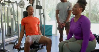 Spor salonunda dambıllarla egzersiz yapan genç bir çift, kişisel antrenör antrenman yapıyor. Fitness, antrenman, koçluk, güç, egzersiz, ağırlık