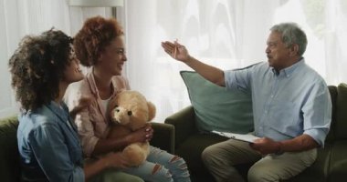 Çift cinsiyetli lezbiyen çift ellerinde oyuncak ayıyla kanepede terapi sırasında gülümsüyorlar. lgbtq, danışmanlık, ilişki, arkadaşlık, ruh sağlığı, destek