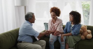 Çift cinsiyetli lezbiyen çift koltukta yaşlı adamla tartışıyor, tablet tutuyorlar, gülümsüyorlar, evde. lgbtq, aile, teknoloji, sohbet, çeşitlilik, nesil farkı