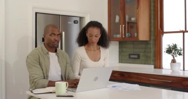 Mutfakta dizüstü bilgisayar kullanan mutlu çift kahve ve belgelerle birlikte plan yapıyor. Takım çalışması, yaşam tarzı, kahvaltı, ilişki, mutluluk, teknoloji