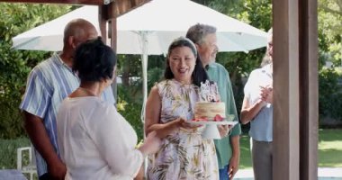 Farklı kıdemli arkadaşlar arka bahçede doğum günü kutluyor, gülümsüyor ve mumlarla pasta tutuyorlar. Kutlamalar, farklı kıdemli arkadaşlar partisi, doğum günü pastası, arka bahçede parti, mutluluk, birliktelik