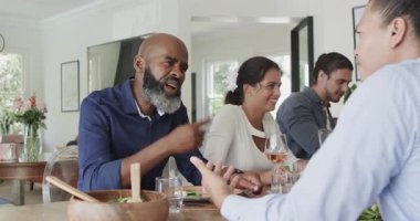 Çeşitli aileler salata kasesini elden alıyor, yemek odasında yemek paylaşıyorlar. Aile toplantısı, toplu yemek, sıcak atmosfer, samimi an, iç mekan, neşe, bağlantı