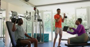 Genç çift spor salonunda egzersiz yapıyor, ağırlık kaldırıyor ve tablet kullanıyor. Fitness, egzersiz, güç, teknoloji, motivasyon, egzersiz