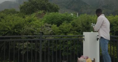 Afro-Amerikalı adam şarap şişesi ve cam kaldırıyor sonra terasa minder ve bardak yerleştiriyor. Açık hava, dinlenme, rahatlama, manzara, tarz, kırsal, huzur.