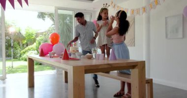 Çeşitli aileler evde pasta, balon ve parti şapkalarıyla doğum günü kutlamalarının tadını çıkarıyor. Kutlama, aile, neşe, etkinlik, mutluluk, dekorasyon, parti, birliktelik