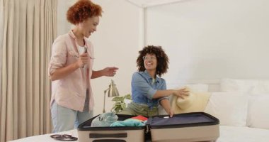 Mutlu lezbiyen çift yataklarında bavullarını topluyor, evde tatil gezisine hazırlanıyorlar. Seyahat, bagaj, planlama, neşe, yatak odası