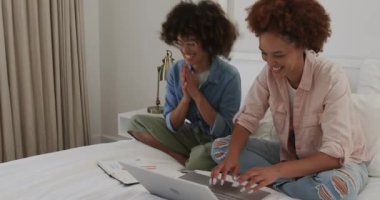 Çift cinsiyetli lezbiyen çift dizüstü bilgisayarlarını yatakta kullanıyor, evde kaliteli vakit geçiriyorlar. LGBTQ, teknoloji, rahatlama, bilgisayar, ilişki, bağ