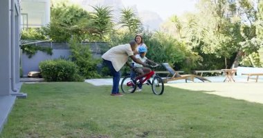 Babası çocuğa güneşli arka bahçede bisiklet sürmeyi öğretiyor, çeşitli aile zamanlarının tadını çıkarıyor. ebeveynlik, bağlanma, açık hava, eğitim, çocukluk, boş zaman