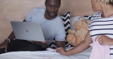 Yatakta dizüstü bilgisayar kullanırken bebek kıyafetlerini tartışan çeşitli çiftler. Aile, ebeveynlik, planlama, online alışveriş, yaşam tarzı, aile içi