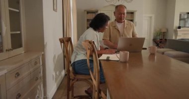 Üst düzey Asyalı çift evde dizüstü bilgisayar kullanıyor, planları tartışıyor ve birlikte kahvenin tadını çıkarıyorlar. Çeşitli yaşlılar, teknoloji, tartışma, yaşam tarzı, planlama