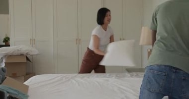 Yeni yatak odasına taşınmak, çeşitli kutuları açmak ve yatak yaparken yorgan sermek. İç mekan, yenileme, takım çalışması, konforlu yaşam tarzı, minimalizm, doku