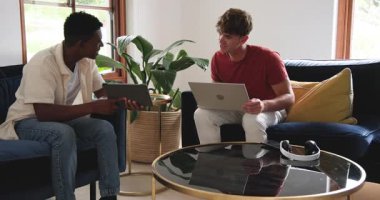 Tablet, erkek iş arkadaşlarını kanepede kurgu yapmak için dizüstü bilgisayarda yazarken tablet çevirmeye sevk ediyor. İşbirliği, takım çalışması, modern, gündelik, teknoloji, iletişim, yenilik