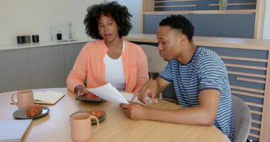 Mutfak masasında kahve ve hamur işleriyle evrakları inceleyen genç bir çift. Evrak işleri, yemek, kahvaltı, ev, yaşam tarzı, ev