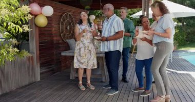 Arka bahçedeki doğum günü kutlamalarının tadını çıkaran çeşitli yaşlılar havuz başında gülümseyip pasta tutuyorlar. yaşlılar, arkadaşlık, mutluluk, parti, eğlence, yaşam tarzı