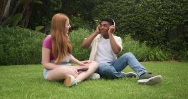 Çeşitli arkadaşlar akıllı telefondan müzik keşfediyor ve arka bahçede kablosuz kulaklık takıyorlar. Açık hava, eğlence, işbirliği, teknoloji, yaşam tarzı, coşku, arkadaşlık