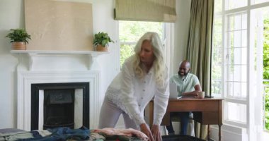 Yaşlı çift yatakta bavul açıyor, giysileri düzenliyor, telefon ve tableti gözden geçiriyor. Aile, yerli, yaşam tarzı, planlama, organizasyon, konforlu, bağlantı