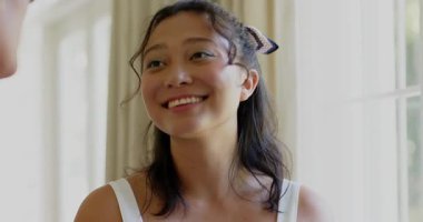 Asyalı bir kadın arkadaşını dinliyor, baş parmaklarına gülümsüyor ve uzun pencerenin yanında başını sallıyor. Dost canlısı, rahat, parlak, samimi, doğal, uyumlu, anlamlı.