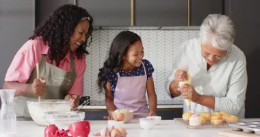 Üç farklı nesil birlikte kek pişiriyor, mutfakta ve evde kahkaha ve neşe paylaşıyor. çesitli aile, birliktelik, mutluluk, çoklu jenerasyon, bağ, kutlama
