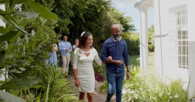 Konukçu, Afrikalı Amerikalı erkek ve Asyalı kadın yürüyen taş yolda, hediye kutusu dağıtıyorlar. Kutlama, açık hava, doğa, zarafet, arkadaşlık, sosyal, toplum