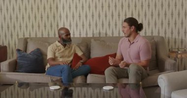 Çeşitli erkek arkadaşlar el sıkışıyor ve bej kanepede konuşan genç arkadaşlardan sonra sarılıyorlar. Arkadaşlık, bağlantı, sıcak, güven, sohbet, jest, destek