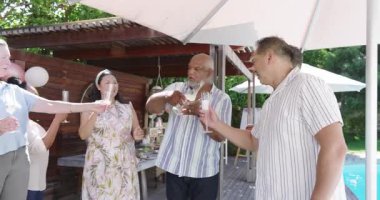 Çeşitli yaşlılar bahçede kutlama yapıyor, kadeh kaldırıyor ve havuz başında kutlama yapıyorlar. Kutlama, kadeh kaldırma, havuz kenarı, çeşitli son sınıf arkadaşları, eğlence.