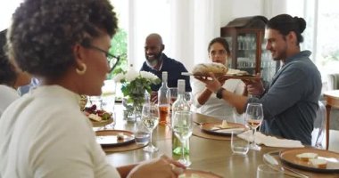 Kadın somun ekmek yerleştirir, ekmek doğrar, gül kızartırken çeşitli aileler ahşap masanın etrafında toplanır. Aileler, kutlamalar, neşe, sade, sıcak, birliktelik, beslenme.