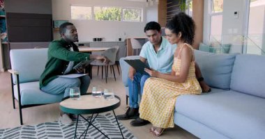 Afro-Amerikalı adam ve çeşitli arkadaşlar evde tablet ve su bardaklarıyla tartışıyorlar. Tartışma, modern, arkadaşlık, teknoloji, gündelik, iletişim, güneş ışığı, dekor