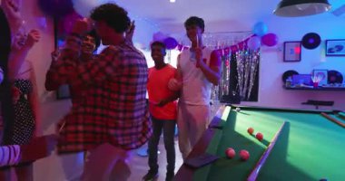 Farklı arkadaşlar müzik çalarken oyun odasında disko topunun altında bilardo oynuyorlar. Kutlama, gece hayatı, hayat dolu, dostluk, eğlence, sosyalleşme, şenlik.