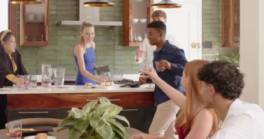 Afro-Amerikan bir adam akıllı telefondan el kol hareketi yaptıktan sonra mutfakta çeşitli arkadaşlar su bardağı kaldırıyor. Yoldaşlık, kutlama, sıcaklık, sosyalleşme, modern, canlı, gayri resmi