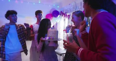 Doğum günü kızı için pasta taşıyan çeşitli arkadaşlar oyun odasında akıllı telefonla mum üflüyorlar. Kutlama, dostluk, coşkulu, neşeli, parti, gündelik, sosyal