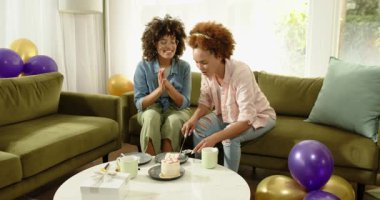 Evde kutlama yapıyorlar, neşeli lezbiyen çift etraflarında balonlarla pasta kesiyorlar. Kutlama, mutluluk, birliktelik, parti, şenlik