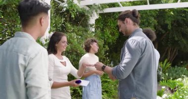 Asyalı bir adam pergola altında kutu teslim etmeyi teklif ediyor, kadın zarfı açıyor, erkek parmağına yüzük takıyor. Romantizm, kutlama, zarafet, samimiyet, açık hava, arkadaşlık, neşe