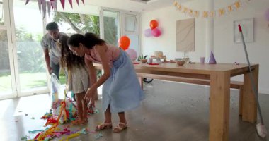 Doğum günü partisi odasındaki renkli konfetileri evde, şenlikli bir dekorla temizleyen farklı bir aile. Kutlama, temizlik, şenlik, aile, eğlence, dekorasyon, balonlar, takım çalışması